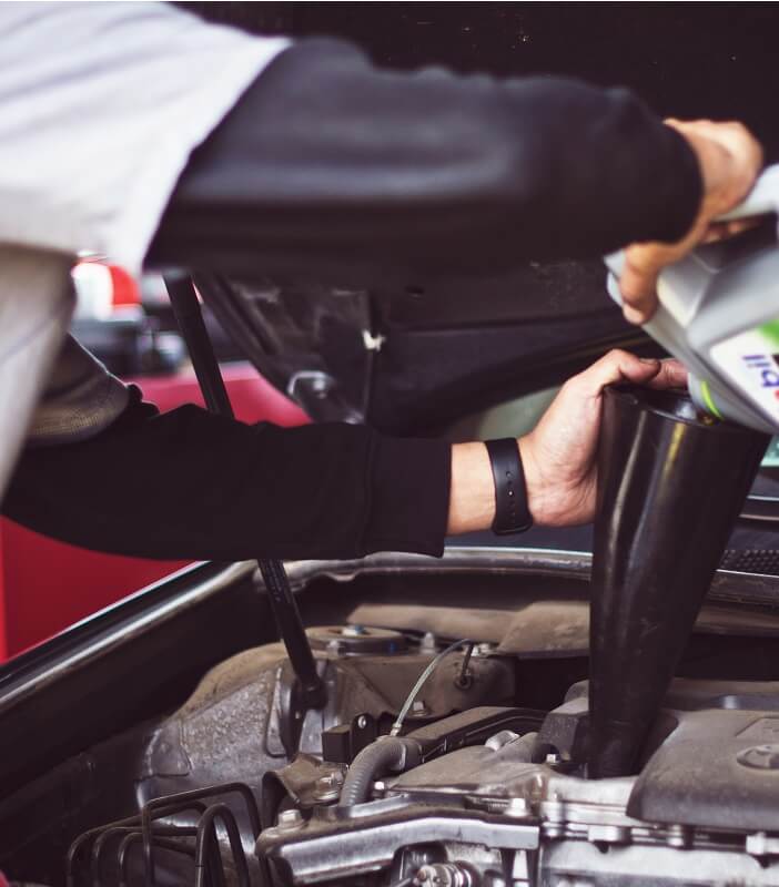 A DIY car repair enthusiast under the hood of a passenger vehicle in the process of completing an oil change.