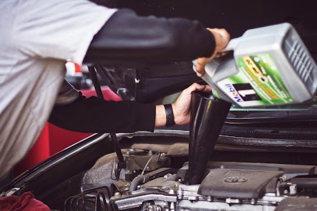 A DIY car repair enthusiast under the hood of a passenger vehicle changing the oil.