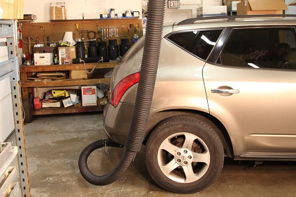 Telesoping exhaust system attached to the tailpipe of a passenger vehicle in a service garage.
