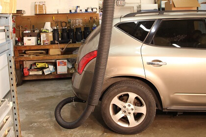 Telesoping exhaust system attached to the tailpipe of a passenger vehicle in a service garage.